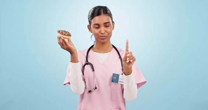 Woman nurse with donut and no gesture for nutrition, wellness or health diet in studio. Upset, medical and portrait of Indian female doctor nutritionist with sweet dessert isolated by blue background
