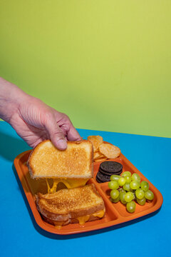 Hand reaches for grilled cheese sandwich on tv tray