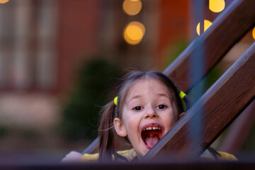 Happy little girl looking at camera with open with joy mouth, standing behind fence from...