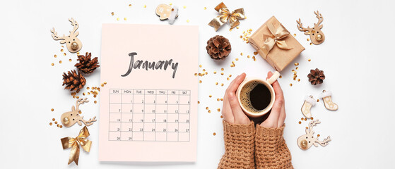 Paper calendar for January with Christmas decorations and female hands with cup of coffee on light background