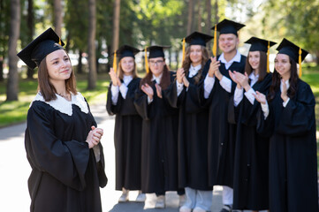 Group of happy students in graduation gowns outdoors. A young girl in the foreground.