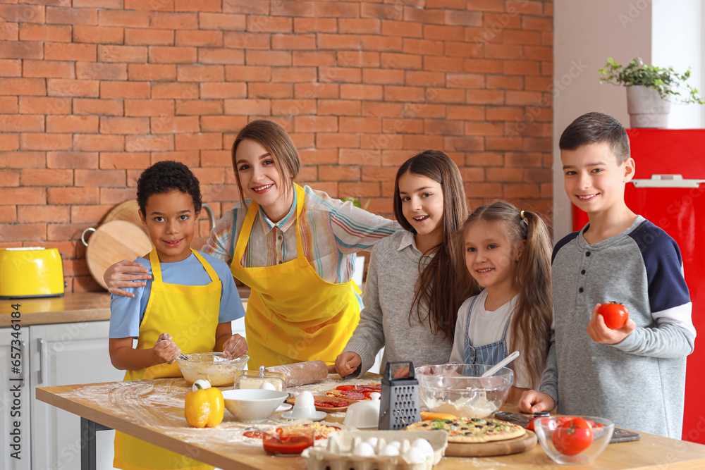 Poster female chef with group of little children preparing pizza during cooking class in kitchen