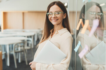 Young beautiful woman wearing stylish eyeglasses holding laptop using sticky notes