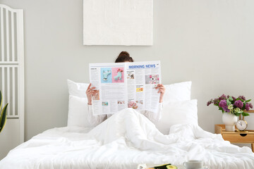 Morning of young woman reading newspaper in bedroom