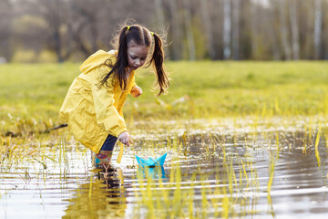 Calm child standing in puddle in lawn, bending over, stretching arm and launching paper ship, playing on fall day.