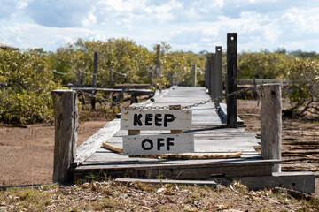 Rustic wooden jetty with “keep off” sign on a tidal creek. Poona, Queensland, Australia
