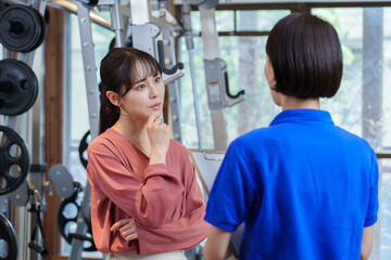 Obraz premium ジムでトレーナーから説明を聞く困った顔をした女性