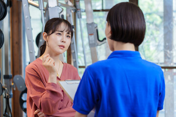 Obraz premium ジムでトレーナーから説明を聞く困った顔をした女性