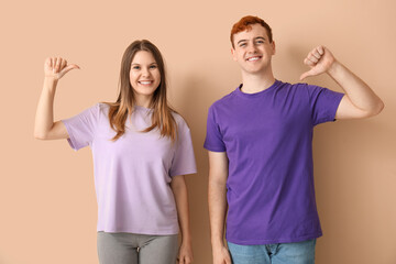 Young couple pointing at their t-shirts on beige background