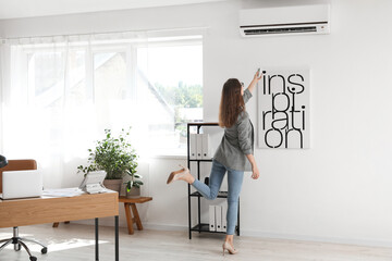 Young businesswoman turning on air conditioner in office