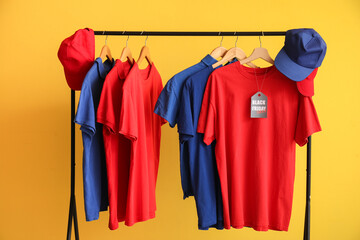 Obraz premium Rack with different t-shirts and caps on yellow background. Black Friday sale