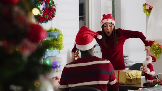 Employee wearing Christmas hat entertaining coworkers by mocking their team leader during break. Staff members having fun doing pantomime during Secret Santa party before xmas