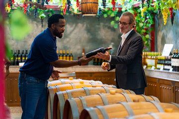 Professional African man wine shop worker explaining and recommending wine to customer at liquor store. Sommelier testing wine in winery. Winery or brewery manufacturing industry and winemaker concept