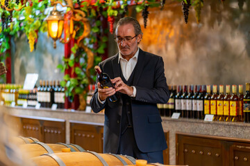 Caucasian senior man choosing and buying wine at wine shop. Sommelier tasting wine at liquor store....