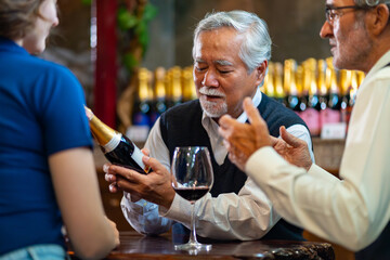 Professional senior man sommelier explaining and recommending wine to customer at wine shop or liquor store. Sommelier tasting wine in winery. Winery manufacturing industry and winemaker concept.