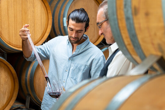 Group of Man and woman sommelier tasting red wine in wooden barrel at vintage wine cellar at wine factory. Winery, wine shop, brewery liquor business manufacturing industry and winemaker concept.
