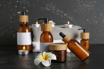 Composition with different cosmetic products, clean towels and burning candles on dark background