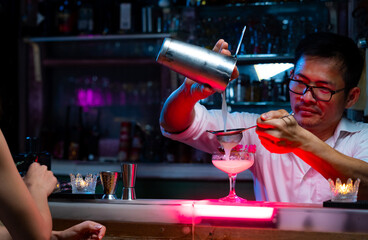 Professional male bartender preparing and serving cocktail drink to customer on bar counter at...