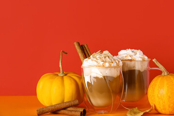 Glasses of tasty pumpkin latte with cinnamon and almond on colorful background