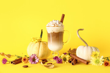 Obraz na płótnie Canvas Glass cup of tasty pumpkin latte with cinnamon and almond on yellow background
