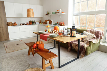 Interior of modern kitchen with served dining table, pumpkins, bench and sofa