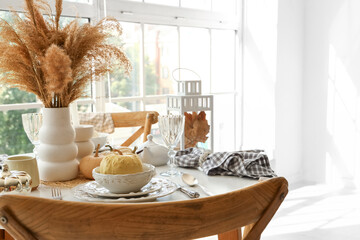 Autumn table setting with pampas grass and pumpkins in light kitchen near big window