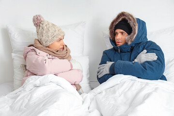 Frozen young couple with puffers lying in bedroom