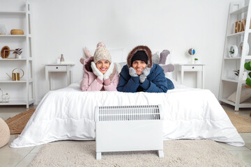 Young couple with puffers warming near radiator in bedroom