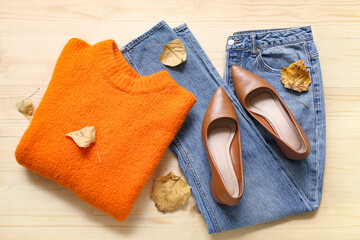 Composition with stylish female clothes, shoes and fallen leaves on wooden background