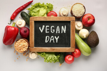 Board with text VEGAN DAY and different healthy products on grey background