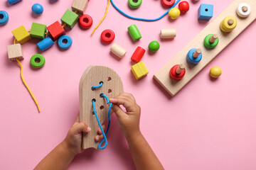 Motor skills development. Little child playing with wooden lacing toy at pink table, top view
