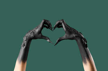 Black hands of witch with claws making heart on green background. Halloween celebration - obrazy, fototapety, plakaty