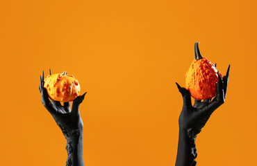 Black hands of witch with pumpkins on orange background. Halloween celebration