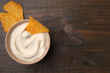 Delicious tofu sauce served with nachos chips in bowl on wooden table, top view. Space for text