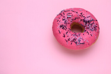 Glazed donut decorated with sprinkles on pink background, top view. Space for text. Tasty...