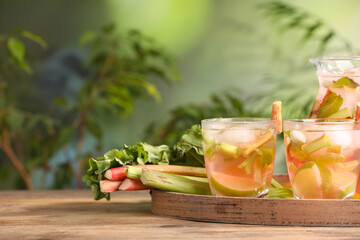Glasses and jug of tasty rhubarb cocktail with citrus fruits on wooden table outdoors, space for text
