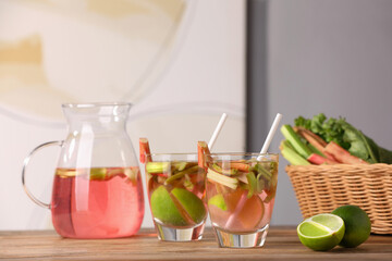 Glasses and jug of tasty rhubarb cocktail with lime fruits on wooden table