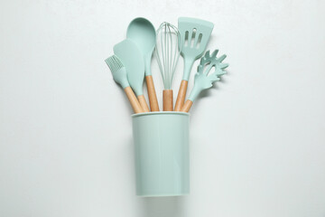 Set of kitchen utensils in holder on white table, top view