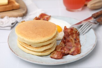 Plate with tasty pancakes, fried egg and bacon on white table, closeup