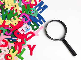 Learning and education concept. Scattered colorful alphabet with a magnifying glass against white...
