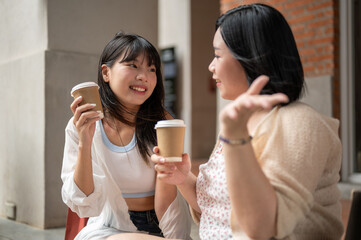 A beautiful Asian woman enjoys talking and having coffee with her friend while sitting on the stairs