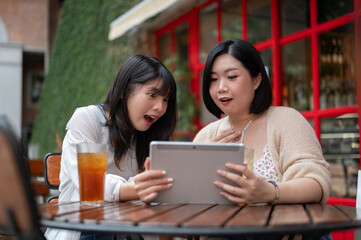 Obraz premium Two surprised Asian female friends are watching an interesting video on a tablet together.