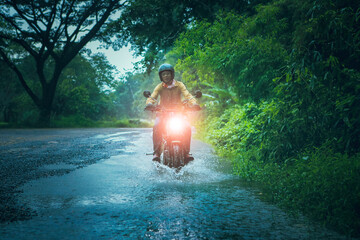man riding small endurom motorcycle crossing shallow creek among rain falling at forest - 657395151