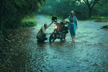 couples of asian biker wearing plastic rain clothes  maintenance small enduro motorcycle in shallow creek among rain falling