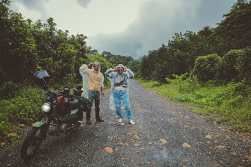 couples of asian biker wearing plastic rain clothes standing beside small enduro motorcycle on country track - obrazy, fototapety, plakaty