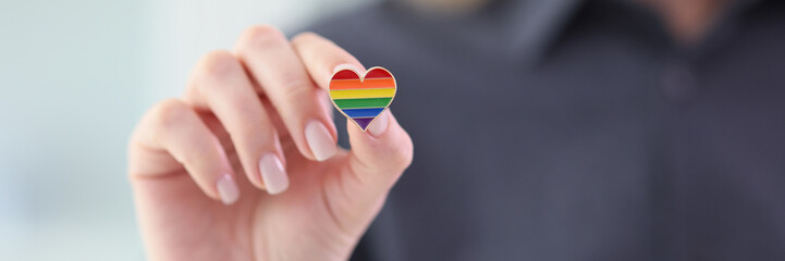 Woman holding small heart with LGBT flag colors closeup