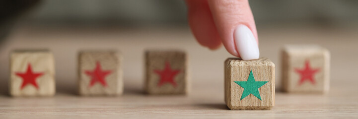 Finger of woman touches kids wooden cube with green star