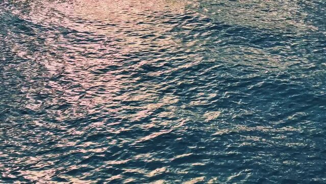 Reflections of the sunset on the surface of turquoise sea water. Caribbean sea texture. Blue sea waves cover the landscape. Flowing clean water in motion. Close up of blue water surface in deep ocean.