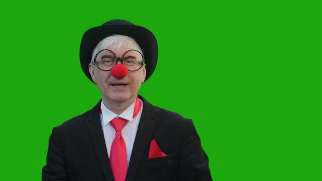 An elderly man in a clown costume laughs, and then takes off his suit and is sad against a green background. Chromakey. 