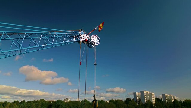 The load block and pulley system of main boom tip sheave on the end of the jib of a blue luffing construction crane. Flag is billowing in the wind. Camera approaching.